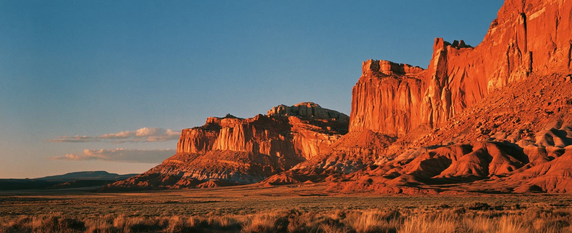 Risograph-style print of high desert badlands at golden hour — red cliffs glowing under a deep blue sky